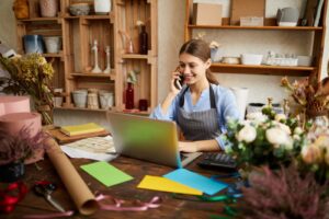 Young small business owner on the phone reviewing her business finances on a laptop